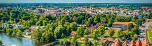 Eine Luftaufnahme der Stadt Lübeck. Zu sehen sind Backsteinhäuser, ein Fluss und die falche Landschaft im Hintergrund.